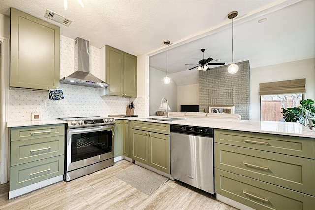 kitchen featuring visible vents, a sink, appliances with stainless steel finishes, wall chimney exhaust hood, and green cabinetry