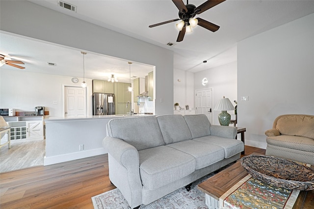 living area with baseboards, a ceiling fan, visible vents, and light wood-type flooring