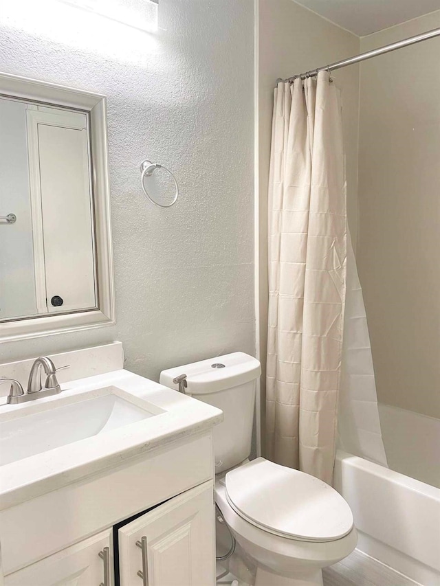 full bathroom featuring toilet, vanity, shower / tub combo, and a textured wall