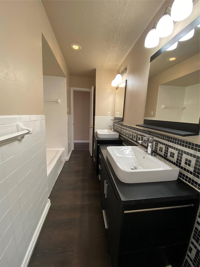 bathroom with a sink, a textured ceiling, double vanity, and a bathtub