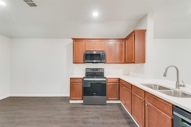 kitchen featuring brown cabinetry, dark wood-style floors, a sink, light countertops, and appliances with stainless steel finishes