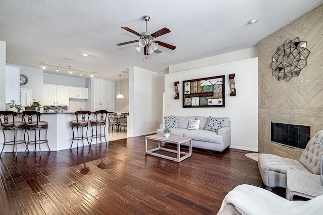 living room featuring dark wood-type flooring, a ceiling fan, a textured ceiling, a fireplace, and baseboards