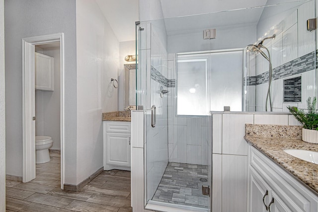 full bath featuring vanity, baseboards, wood tiled floor, a shower stall, and toilet