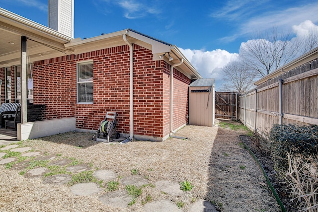 view of side of property with brick siding, an outdoor structure, a chimney, and fence