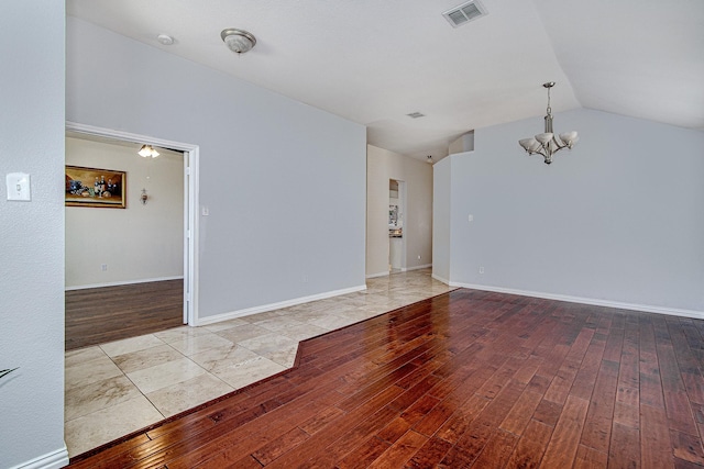 empty room featuring visible vents, a notable chandelier, wood-type flooring, baseboards, and vaulted ceiling