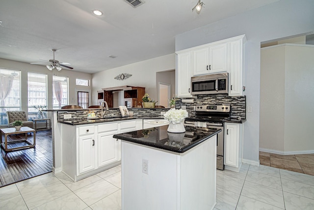 kitchen featuring a center island, open floor plan, a peninsula, stainless steel appliances, and a sink