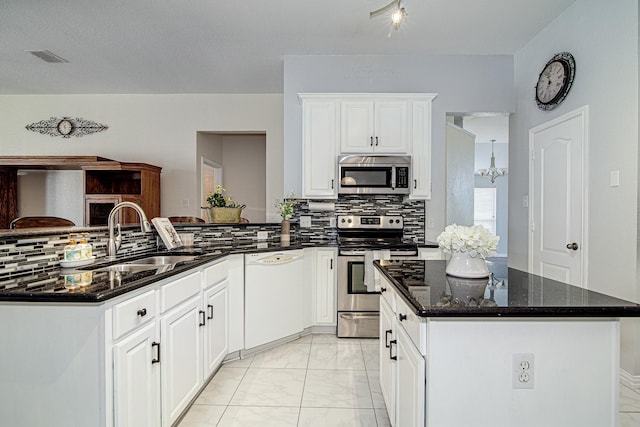 kitchen with dark stone counters, a peninsula, a sink, appliances with stainless steel finishes, and tasteful backsplash