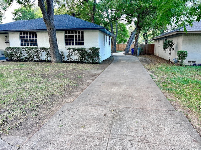 view of property exterior with fence, roof with shingles, concrete driveway, crawl space, and brick siding