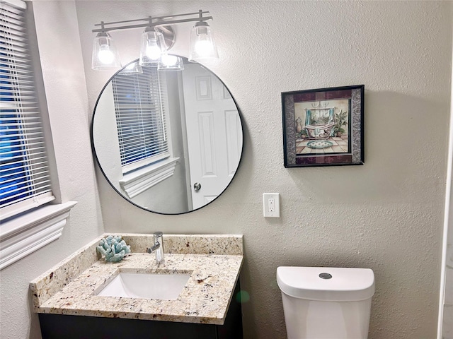 half bathroom with vanity, toilet, and a textured wall