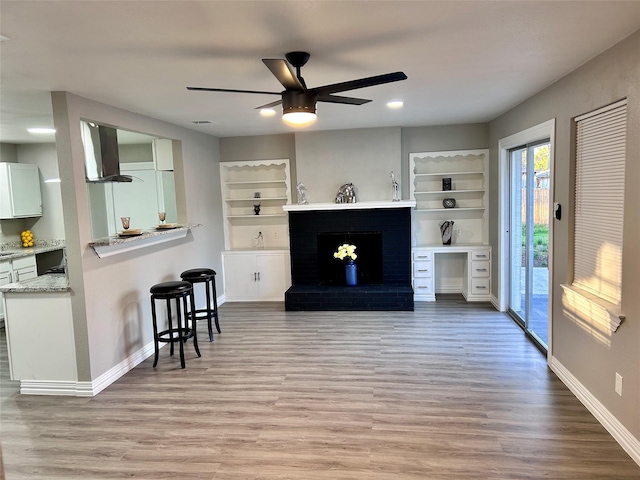 living area featuring a brick fireplace, light wood-style flooring, a ceiling fan, and baseboards