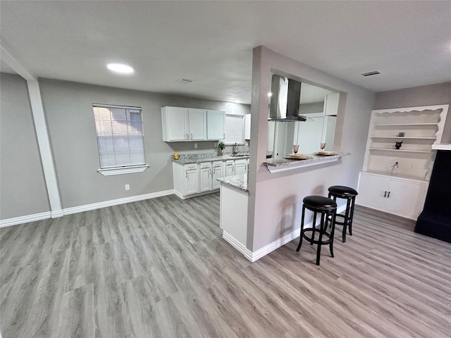 kitchen featuring visible vents, baseboards, wall chimney range hood, a breakfast bar, and light wood-style floors