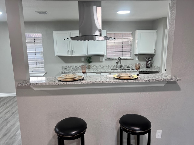 kitchen with visible vents, a kitchen bar, island exhaust hood, white cabinets, and a sink