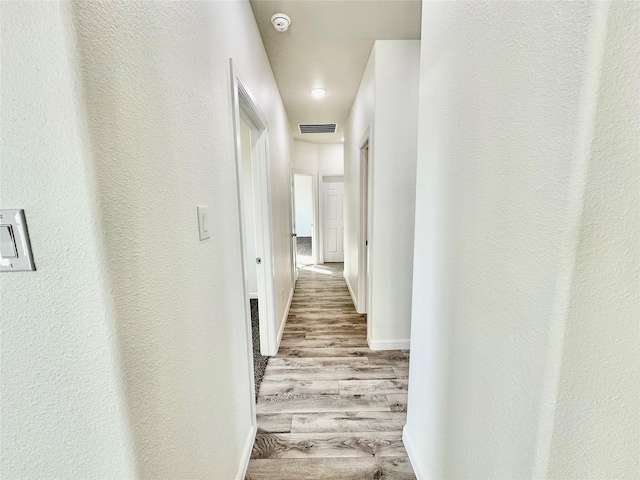 hallway with visible vents, baseboards, and wood finished floors