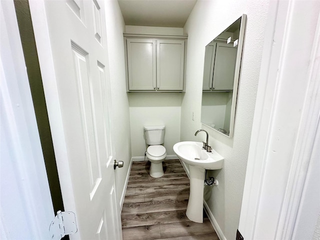 half bathroom featuring toilet, baseboards, and wood finished floors