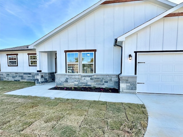 modern farmhouse style home with stone siding, board and batten siding, an attached garage, and a front lawn