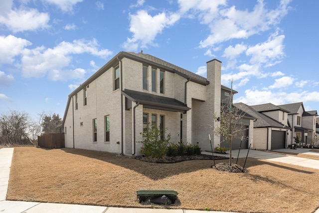 view of front of home featuring brick siding, an attached garage, a chimney, and driveway