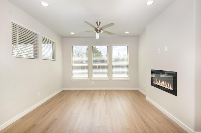 unfurnished living room featuring recessed lighting, light wood-style flooring, baseboards, and a glass covered fireplace