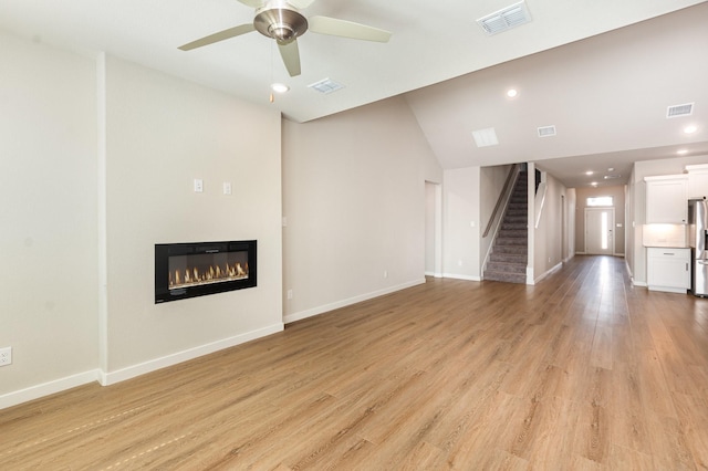 unfurnished living room with a glass covered fireplace, stairway, light wood-style floors, and visible vents