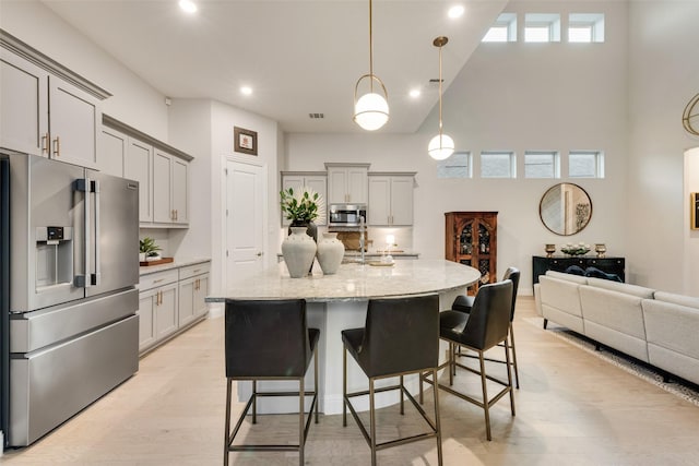 kitchen featuring light wood finished floors, light stone countertops, a kitchen bar, a high ceiling, and stainless steel appliances