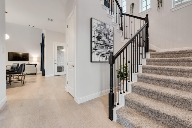 stairway featuring a towering ceiling, baseboards, and wood finished floors