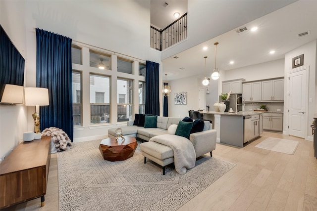 living room with visible vents, recessed lighting, light wood-type flooring, and a towering ceiling