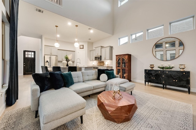 living room featuring a high ceiling, light wood-style floors, visible vents, and baseboards