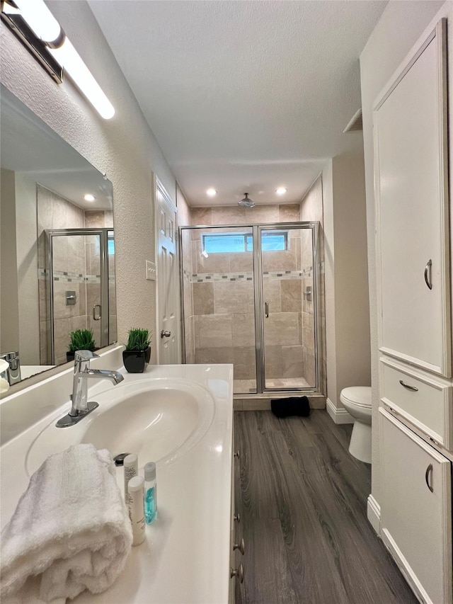 bathroom with a shower stall, toilet, vanity, wood finished floors, and a textured ceiling