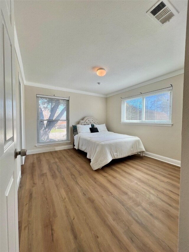 bedroom with visible vents, crown molding, baseboards, and wood finished floors