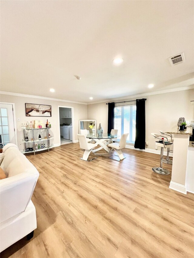 living room featuring light wood-type flooring, visible vents, baseboards, and ornamental molding