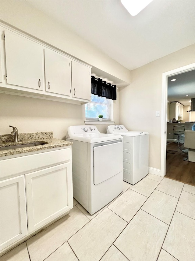 laundry room with light tile patterned floors, baseboards, washing machine and clothes dryer, cabinet space, and a sink