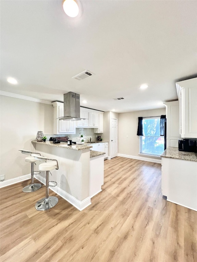 kitchen featuring range hood, a breakfast bar area, a peninsula, white cabinets, and light wood-style floors