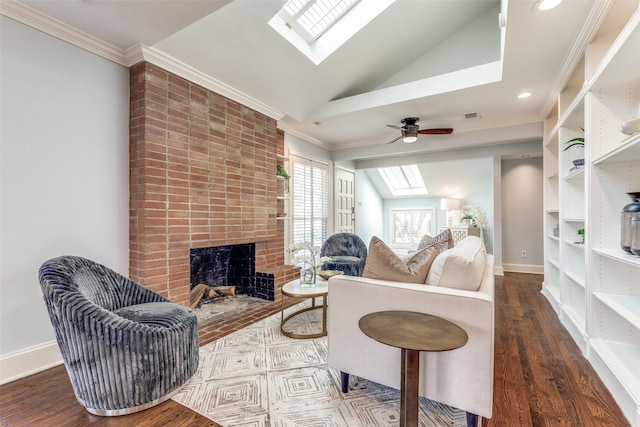 living room featuring wood finished floors, baseboards, vaulted ceiling with skylight, a fireplace, and ornamental molding