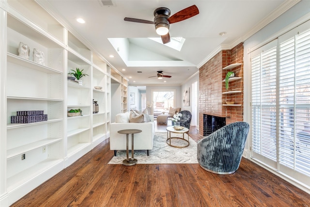 sitting room featuring crown molding, lofted ceiling with skylight, built in features, a fireplace, and wood finished floors