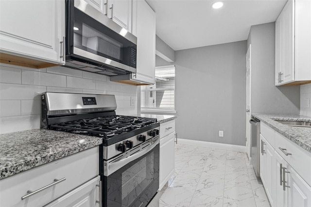 kitchen with baseboards, white cabinets, appliances with stainless steel finishes, marble finish floor, and backsplash