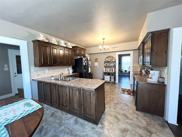 kitchen with a sink, stainless steel appliances, dark brown cabinetry, an inviting chandelier, and a peninsula