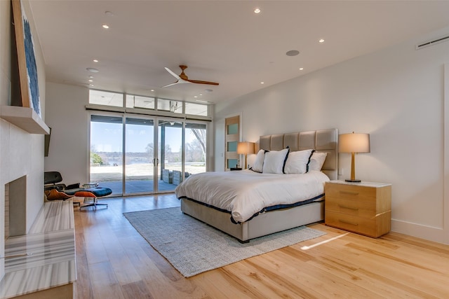 bedroom with a large fireplace, baseboards, recessed lighting, light wood-style flooring, and access to outside