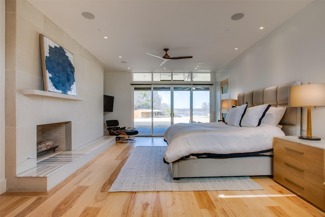 bedroom with a ceiling fan, recessed lighting, light wood finished floors, access to exterior, and a tile fireplace