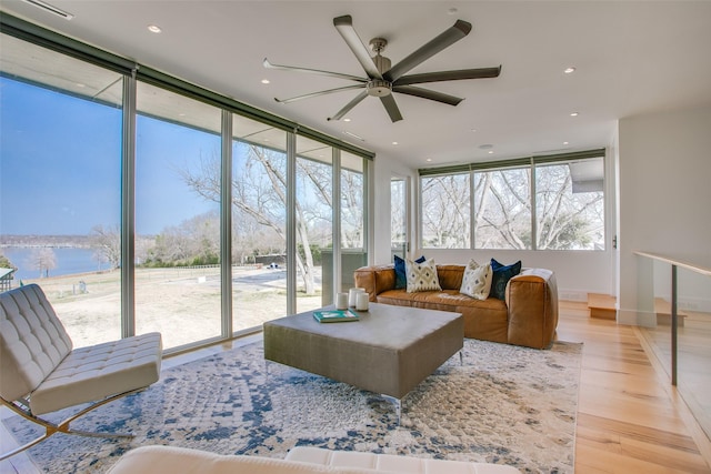 living area with light wood-type flooring, a ceiling fan, recessed lighting, a wall of windows, and baseboards