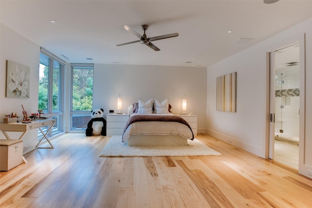 bedroom with wood finished floors, baseboards, ceiling fan, ensuite bathroom, and expansive windows