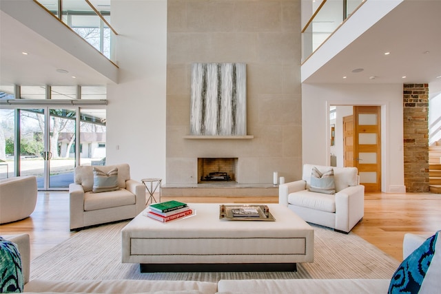 living area with recessed lighting, wood finished floors, a towering ceiling, and a tile fireplace