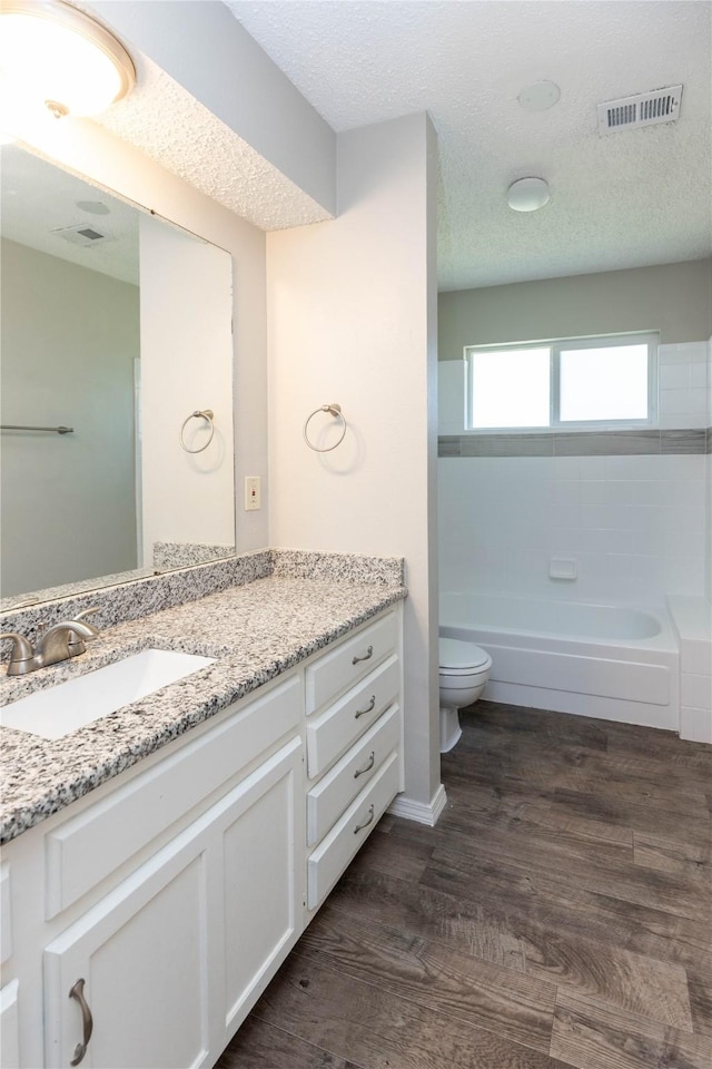 bathroom featuring visible vents, toilet, wood finished floors, and a textured ceiling