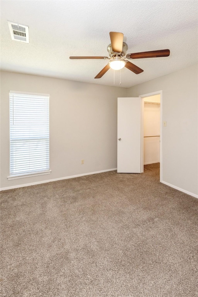 spare room with carpet, baseboards, visible vents, ceiling fan, and a textured ceiling