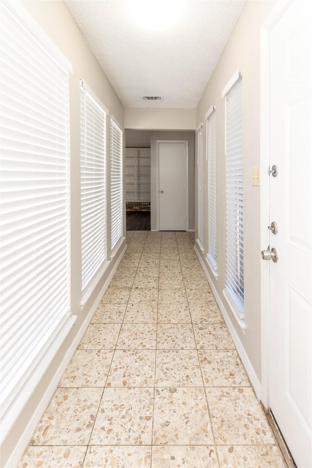 hall with tile patterned floors, baseboards, visible vents, and a textured ceiling