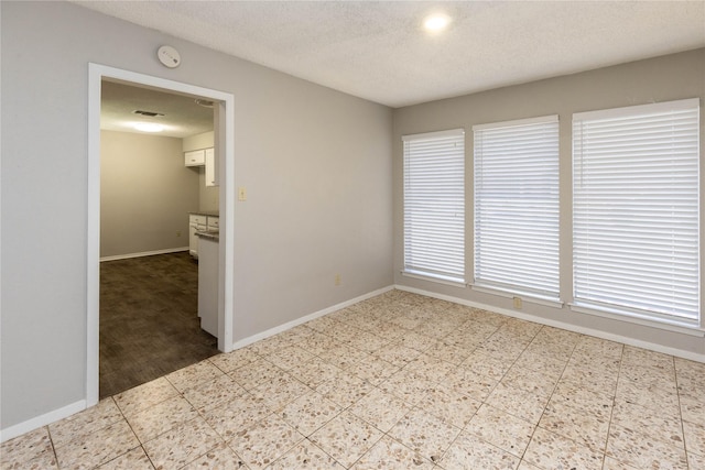 unfurnished room featuring tile patterned floors, baseboards, and a textured ceiling