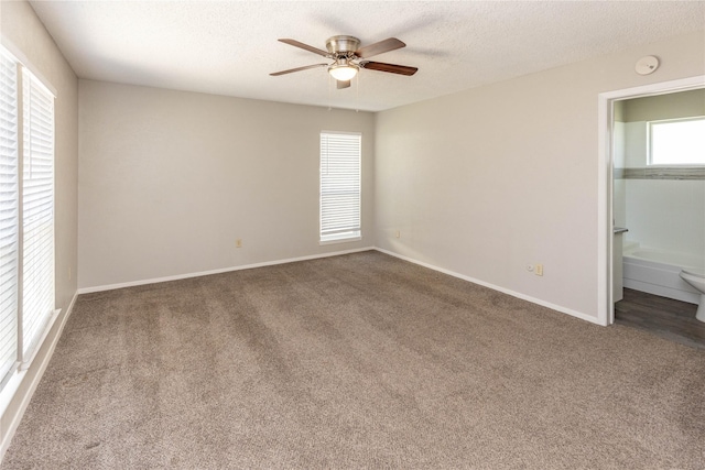 unfurnished bedroom featuring a ceiling fan, baseboards, carpet floors, ensuite bath, and a textured ceiling