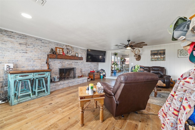 living area with visible vents, a ceiling fan, wood finished floors, brick wall, and a brick fireplace