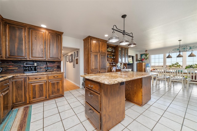 kitchen featuring light tile patterned floors, light stone countertops, decorative backsplash, hanging light fixtures, and a center island