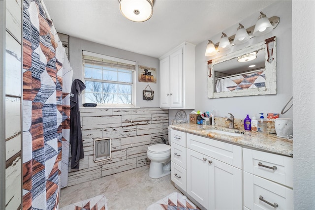 bathroom with vanity, tile walls, toilet, and a wainscoted wall