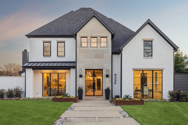 back of house at dusk featuring a standing seam roof, a lawn, brick siding, and metal roof