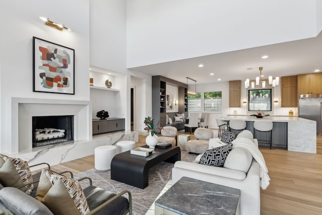 living area featuring light wood-style flooring, built in features, recessed lighting, an inviting chandelier, and a premium fireplace